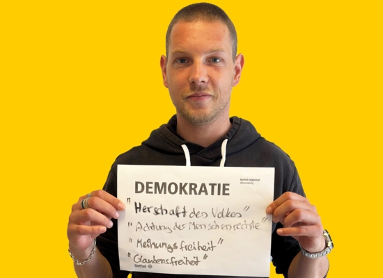 Mann mit Schild in der Hand Demokratie "Herrschaft des Volkes" "Achtung der Menschenrechte" "Meinungsfreiheit" "Glaubensfreiheit".