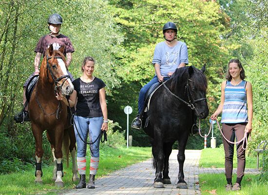 Therapeutisches Reiten: Gruppe von Betreuern und Klienten auf Pferden