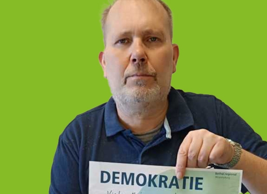 Mann mit Schild in der Hand Demokratie Viele Meinungen unter einen Hut bringen und sich auf Kompromisse einlassen.