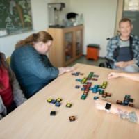 Vier Personen sitzen an einem Tisch und spielen gemeinsam ein Gesellschaftsspiel.