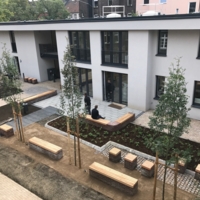 Menschen sitzen im Garten auf Bänken. Im Hintergrund ist die Rückansicht des Hauses in der Zeppelinstraße zu sehen.